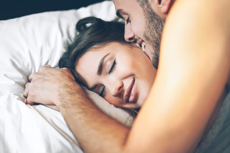 a couple lay together in bed after sex and pleasuring eachother